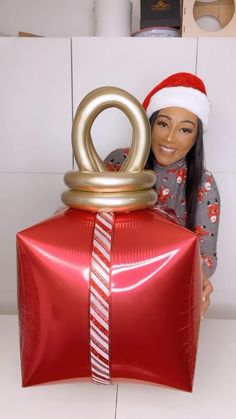 a woman holding a large red present wrapped in foil and wearing a santa claus hat