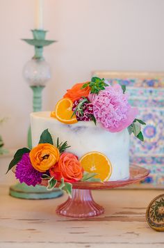 a white cake with oranges and pink flowers on it sitting on top of a table