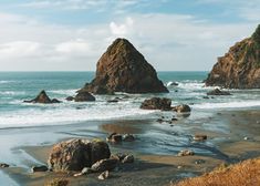 two large rocks sitting on top of a beach next to the ocean