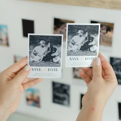 two people holding up small cards in front of pictures on the wall with photos behind them