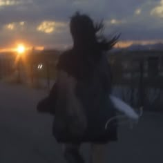 a blurry image of a woman walking down the street at sunset with her hair blowing in the wind