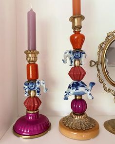 two colorful candlesticks sitting next to each other on a white shelf with a mirror in the background