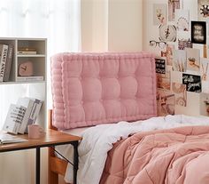 a bed with pink comforter and pillows in a bedroom next to a book shelf