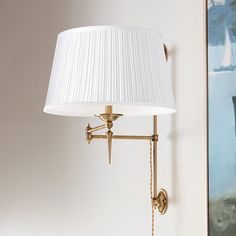 a wall lamp with a white shade on it and a painting in the corner behind it