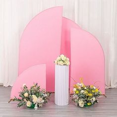 three white vases with yellow and white flowers in front of a large pink sculpture