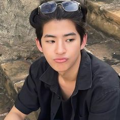 a young man with sunglasses on his head sitting in front of some rocks and looking at the camera