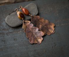 two leaf shaped earrings sitting on top of some rocks