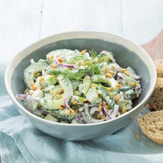 a white bowl filled with cucumber salad next to two slices of bread