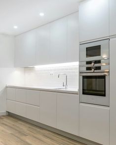 a kitchen with white cabinets and an oven in the center, along with hardwood flooring