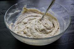 a glass bowl filled with batter on top of a wooden table next to a metal spoon