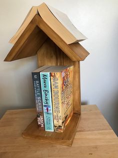 a wooden house shaped like a book shelf with three books in front of it on top of a table