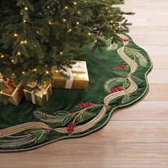 a christmas tree with presents under it on a green area rug next to a lit christmas tree