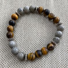 Tiger's Eye and gray Jasper gemstones are accentuated by silver plated spacer beads in this energy bracelet. Wear one or stack them for a unique and artful look. Makes a great birthday, Christmas or graduation gift. Customize with your choice of charms at just $4 each (see photo and order using the link below).Please be sure to choose your size correctly. Use a flat measuring tape around the wrist or see link below. Handmade by Native American Indian Artist/Designer Loren Lavine, in her San Dieg Gray Round Beads Spiritual Bracelet, Adjustable Gray Spiritual Beaded Bracelets, Adjustable Gray Beaded Spiritual Bracelets, Spiritual Gray Beaded Bracelets With 8mm Beads, Adjustable Gray Beaded Bracelets With Natural Stones, Hipster Gifts, Energy Protection, Bracelet Elegant, Boho Men