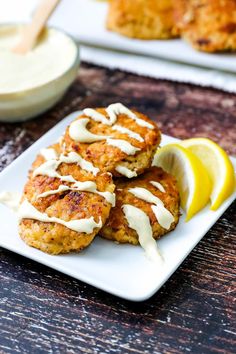 three crab cakes on a white plate with lemon wedges and mayonnaise drizzled over them