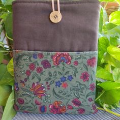 a green and brown bag with flowers on it sitting in front of some greenery