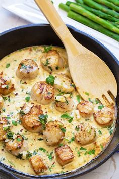 a skillet filled with scallops and sauce next to green asparagus