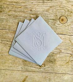 four napkins with monogrammed initials on them sitting on a wooden table top