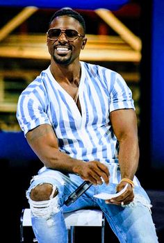 a man sitting on top of a white chair with his legs crossed and wearing ripped jeans