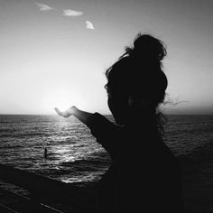 the silhouette of a woman holding her hand out towards the ocean at sunset or sunrise