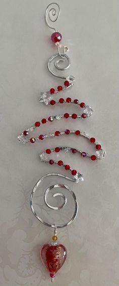 a christmas tree made out of glass beads and silver wire with a red heart hanging from it