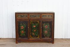 an old wooden cabinet with flowers painted on the front and side panels, sitting against a white wall