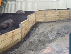 a wooden fence is in the middle of a yard with rocks and dirt around it