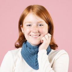 a woman with red hair wearing a blue knitted cowl and smiling at the camera