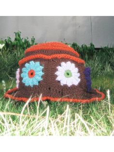 a crocheted hat sitting in the grass with flowers on it's brim