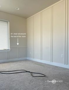 an empty room with white paneling and a black cord on the floor in front of it