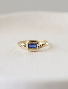 a gold ring with a blue stone in the center on a white surface, close up