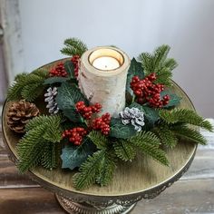 a candle is sitting on top of a table with pine cones and holly wreaths