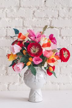 a vase filled with lots of colorful flowers on top of a white table next to a brick wall