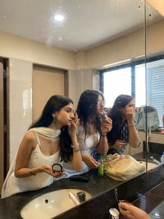 three women are brushing their teeth in front of the bathroom mirror while another woman takes a photo