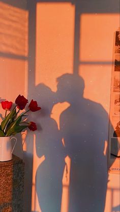 the shadow of a person standing next to a vase with flowers in it