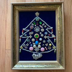 a christmas tree made out of beads and other items in a gold frame on a wooden floor