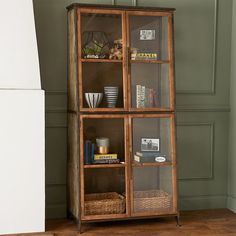 an old wooden bookcase with glass doors and baskets on the bottom shelf next to it