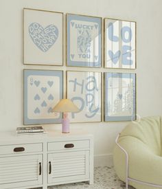 four framed pictures hang on the wall above a white table with a pink lamp in front of it