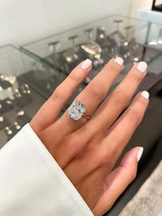 a woman's hand with a diamond ring on top of her finger and some jewelry in the background