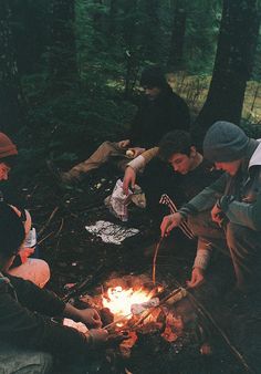 three men sitting around a campfire cooking food