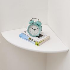 a blue alarm clock sitting on top of a white shelf next to a stack of books