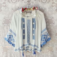 Our Tieton Blouse is sure to be a favorite in your boutique. Gorgeous sky blue embroidery adorns this gorgeous silk boho blouse. Detailed with a smocked neck, tassel tie, draped fit, and embroidery throughout. Custom made to order. Please allow 2 weeks for production. Color: White & sky blue 100% raw silk Imported Hand wash cold split One Size Bust 38 Waist 38 Hips 40 Length 24 Bust, waist, and hip measurements are a total circumference. Length is measured from the top of the blouse to the h White Boho Blouse, Lace Blouses, Bohemian Tunics, Flowy Design, Blouse Price, Boho Blouse, Blue Embroidery, Top Beauty Products, Beautiful Blouses