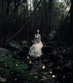 a woman in a white dress is walking through the woods with candles on her feet