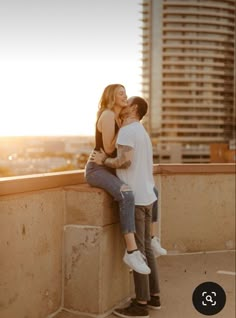 a couple cuddles on the edge of a high rise balcony as the sun sets