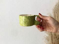 a hand holding a green coffee cup in front of a white wall and fuzzy carpet