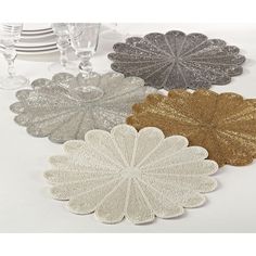 four silver, gold and white plates on a table with wine glasses in the background