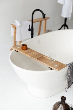 a white bath tub sitting next to a towel rack and wine glass on top of it