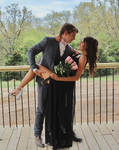 a man in a tuxedo is holding a woman on his back while she holds flowers