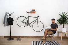 a man sitting in a chair reading a book next to a bike mounted on the wall