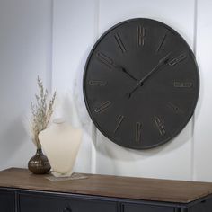 a black clock sitting on top of a wooden table next to a vase with flowers