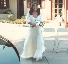 a woman in a white dress standing next to a car